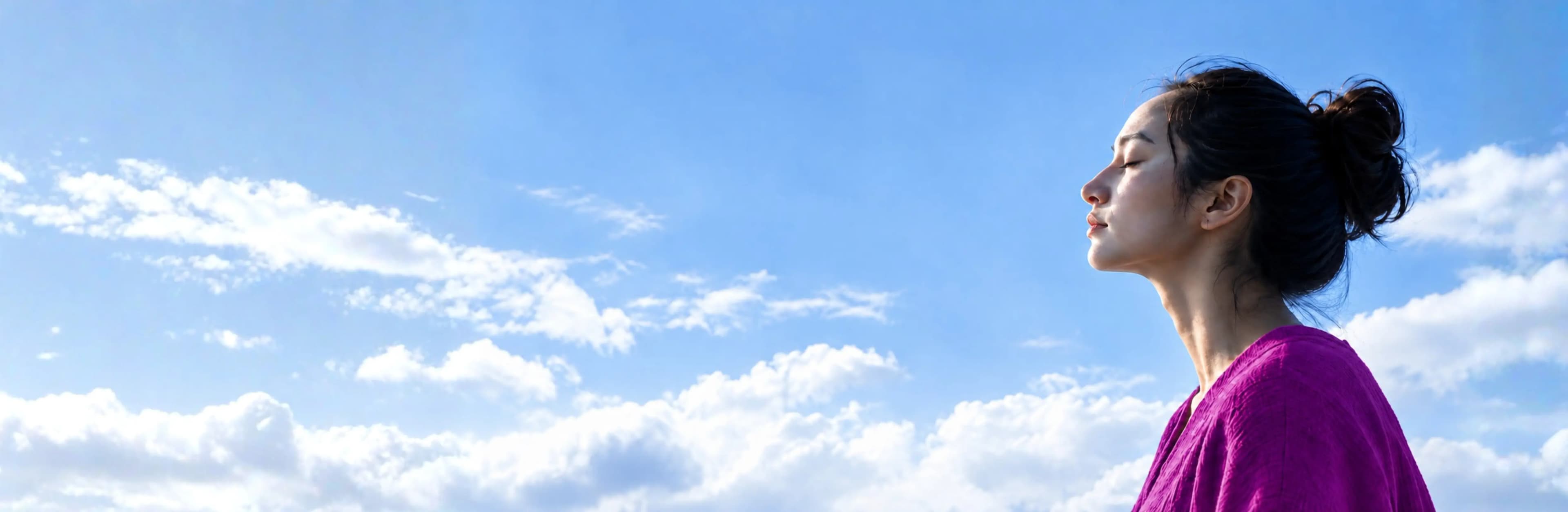 A woman taking a quiet moment beneath a blue sky and white clouds.